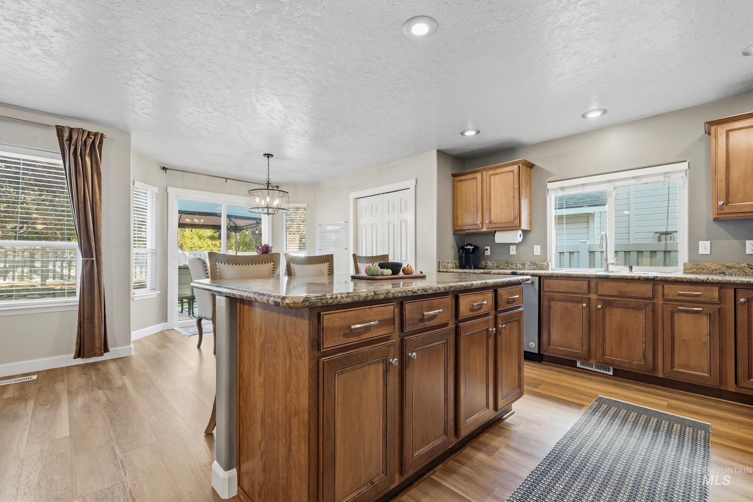 Kitchen with dark stone countertops, a textured ceiling, a kitchen island, light wood finished floors, and recessed lighting