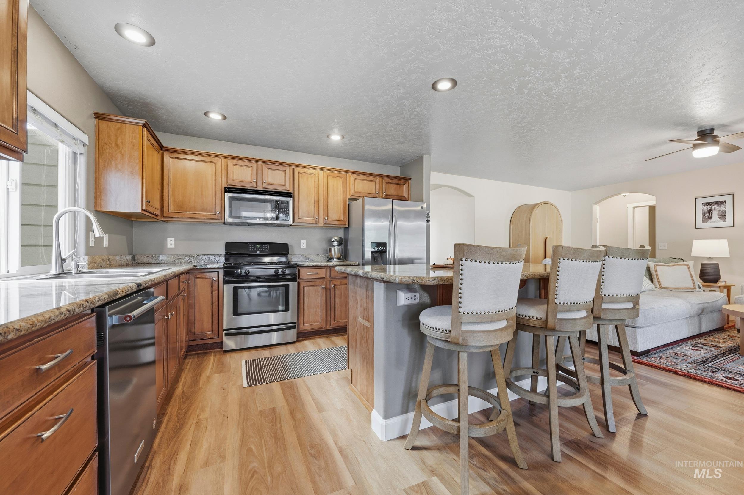 Kitchen featuring light wood finished floors, a kitchen bar, stainless steel appliances, light stone countertops, and a center island