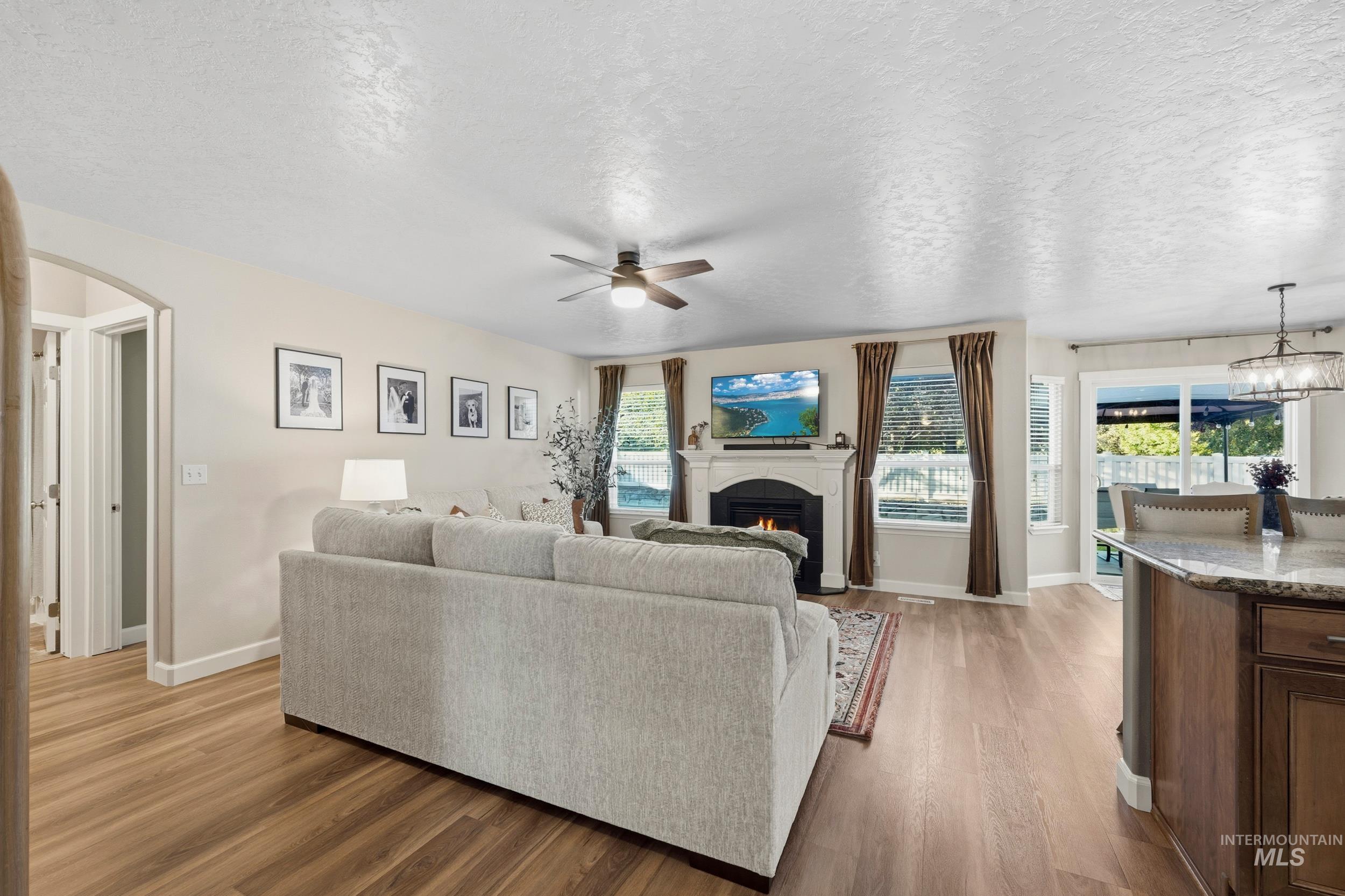 Living room with a textured ceiling, light wood finished floors, arched walkways, a ceiling fan, and a warm lit fireplace