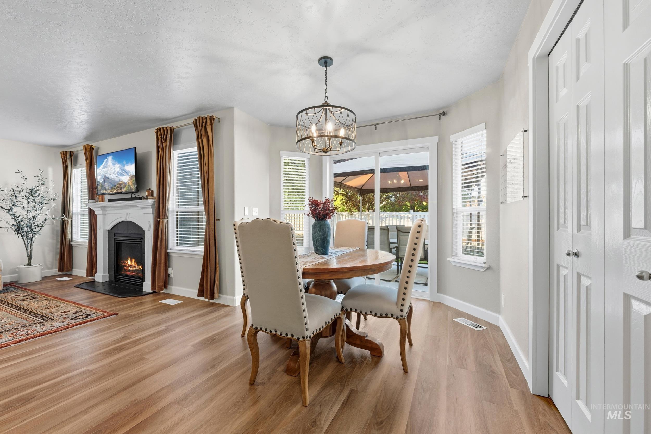 Dining area with a warm lit fireplace, light wood-style flooring, a chandelier, and a textured ceiling
