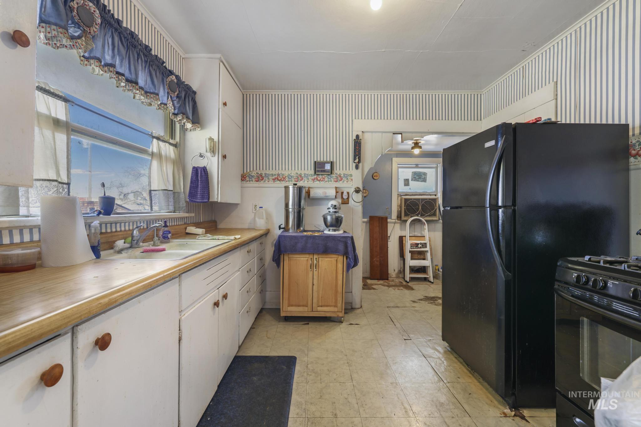 Kitchen featuring white cabinets, black appliances, light countertops, light floors, and wallpapered walls