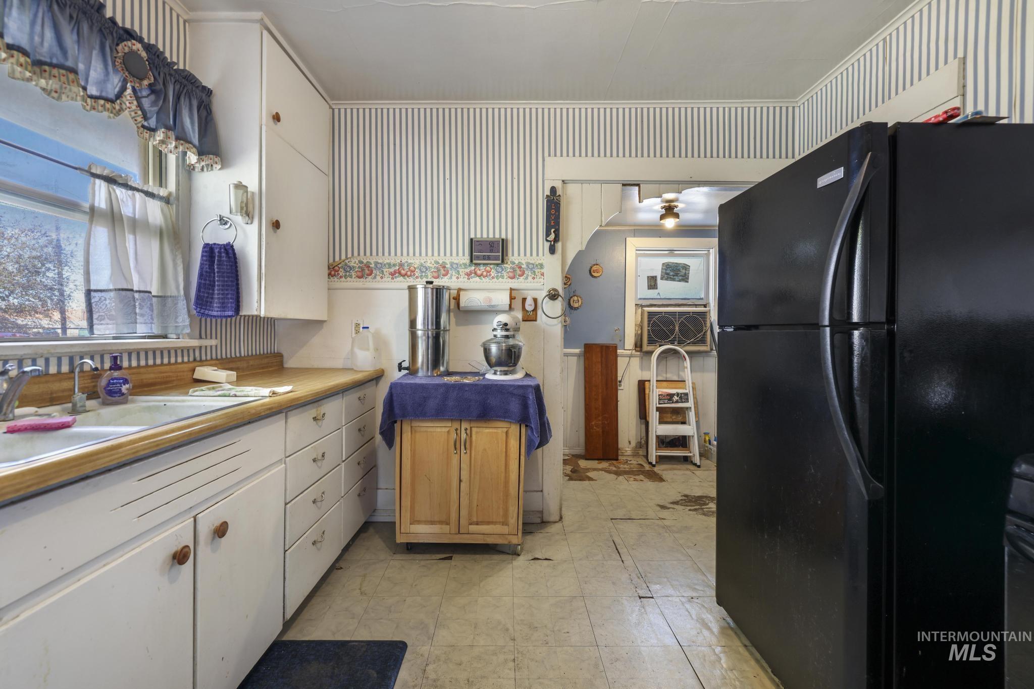 Kitchen featuring freestanding refrigerator, light countertops, white cabinetry, and light flooring