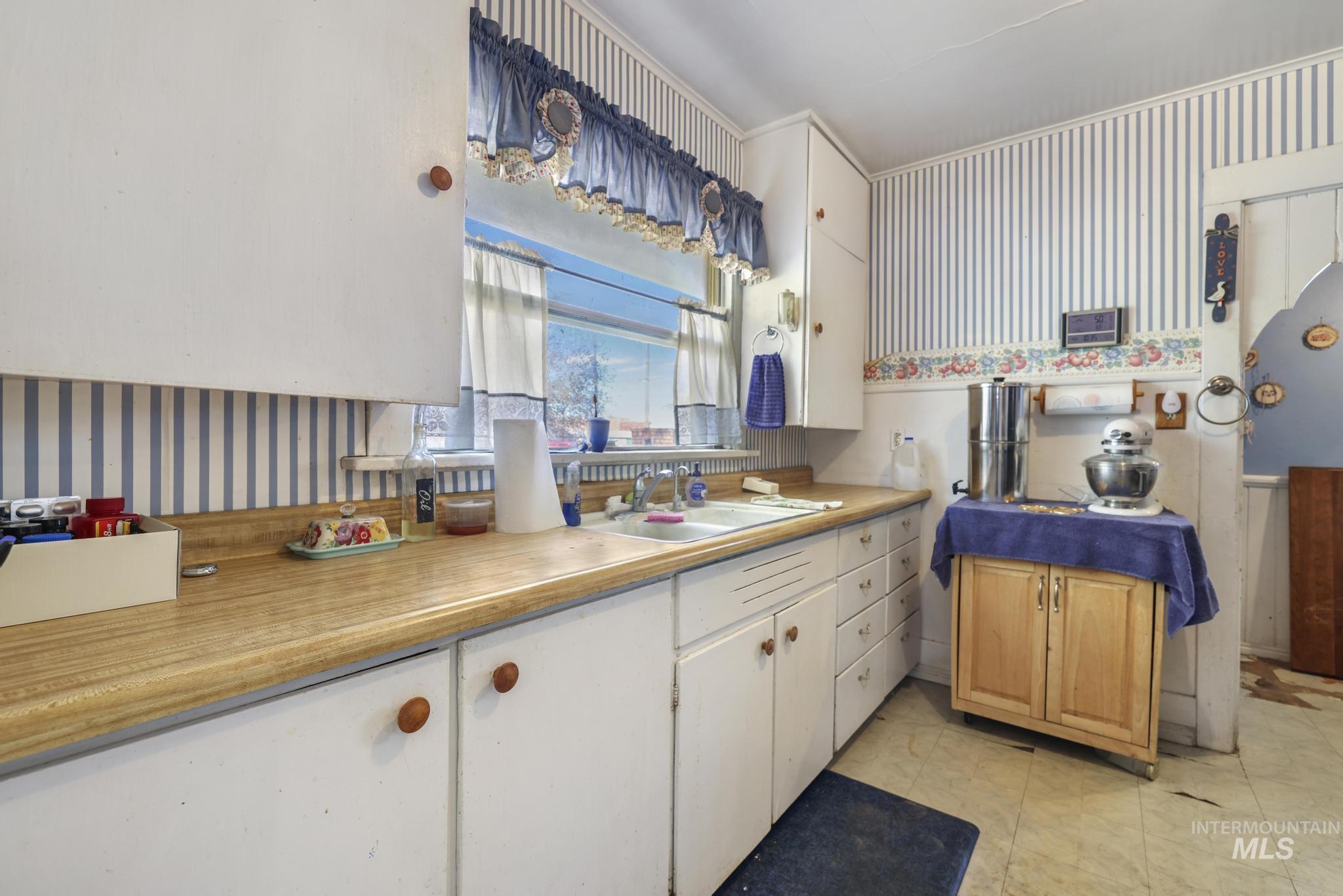 Kitchen with wallpapered walls, light countertops, and white cabinets