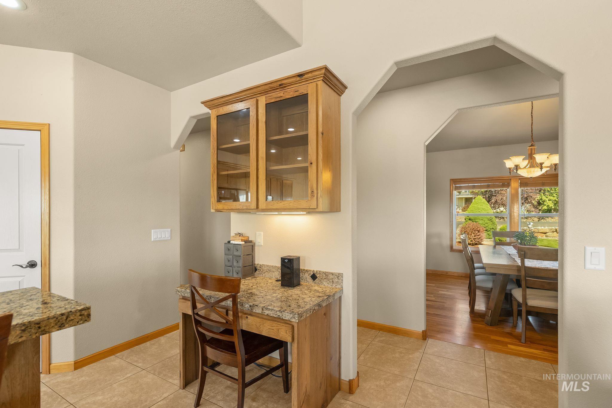 Built-in desk area featuring a stone-finish countertop, upper cabinetry with glass inserts, and task lighting
