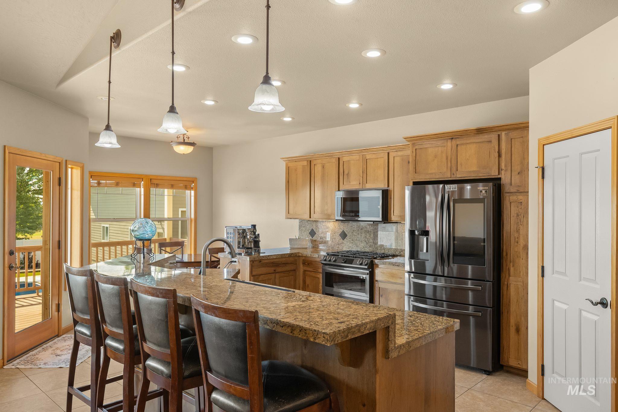 Kitchen featuring an expansive island with a breakfast bar, recessed lighting, wood cabinetry, stainless steel appliances, and a glass-paneled door