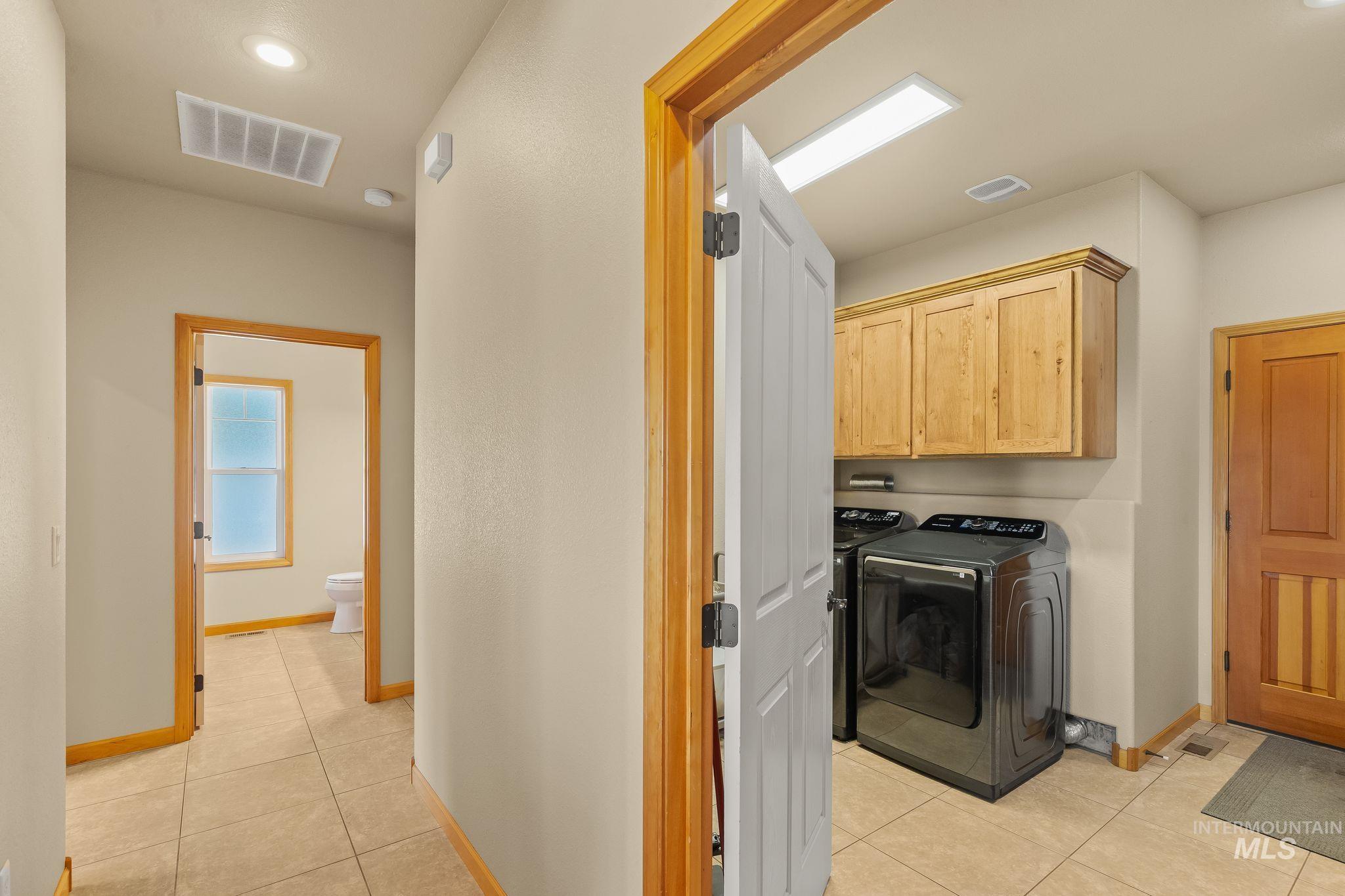 Laundry area featuring wood-finish cabinetry, tile flooring, and integrated lighting