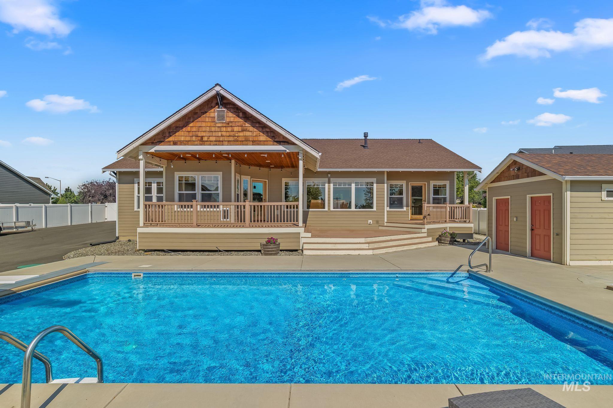 Rear exterior featuring an inground swimming pool, expansive patio, covered porch with wood-look decking, additional wood-look deck area, and a detached auxiliary building