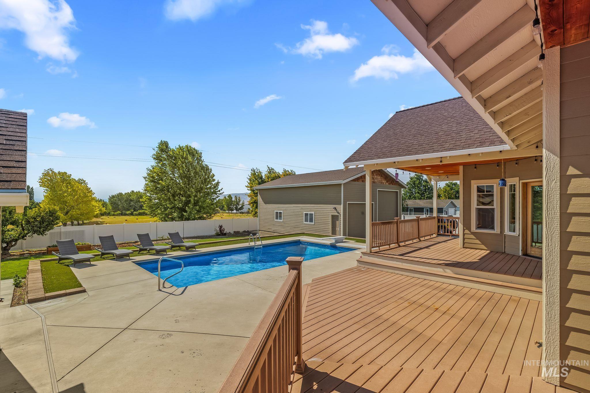 Expansive outdoor living area featuring a large swimming pool with concrete surround, multi-level composite decking, a covered patio with exposed rafters, and a detached two-story outbuilding