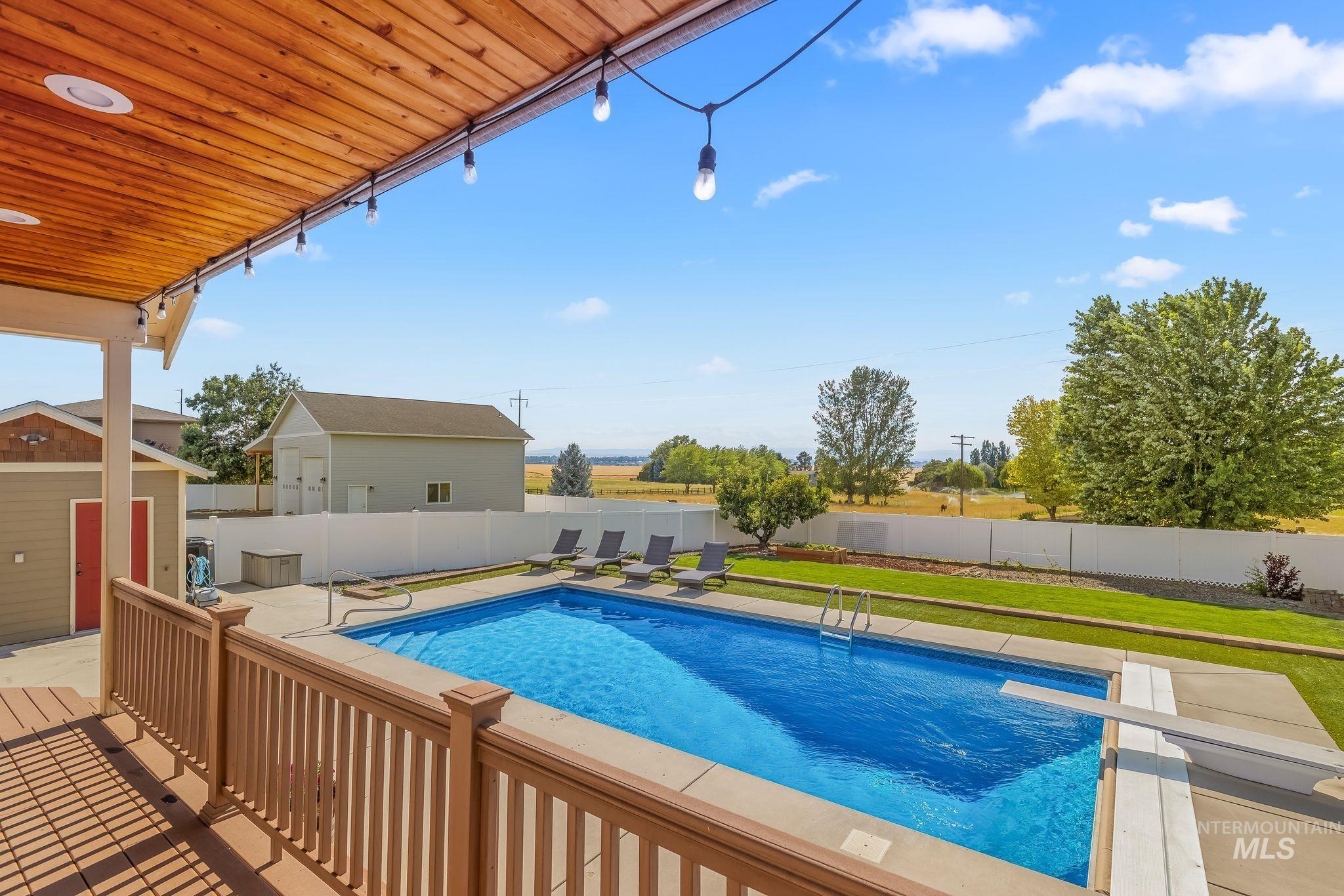 Expansive outdoor living area featuring a covered deck with wood-finish ceiling, an in-ground swimming pool with diving board, a surrounding concrete patio, and a manicured lawn