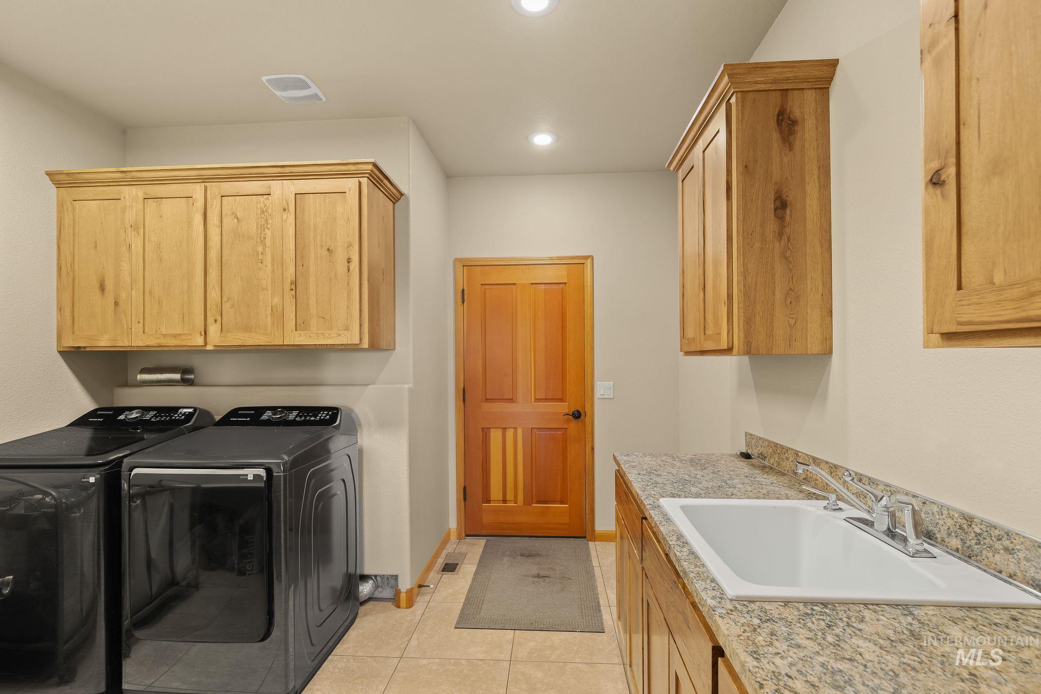 Laundry room featuring tile flooring, wood-finish cabinetry, a utility sink with granite-look countertop, recessed lighting, and a wood-finish door