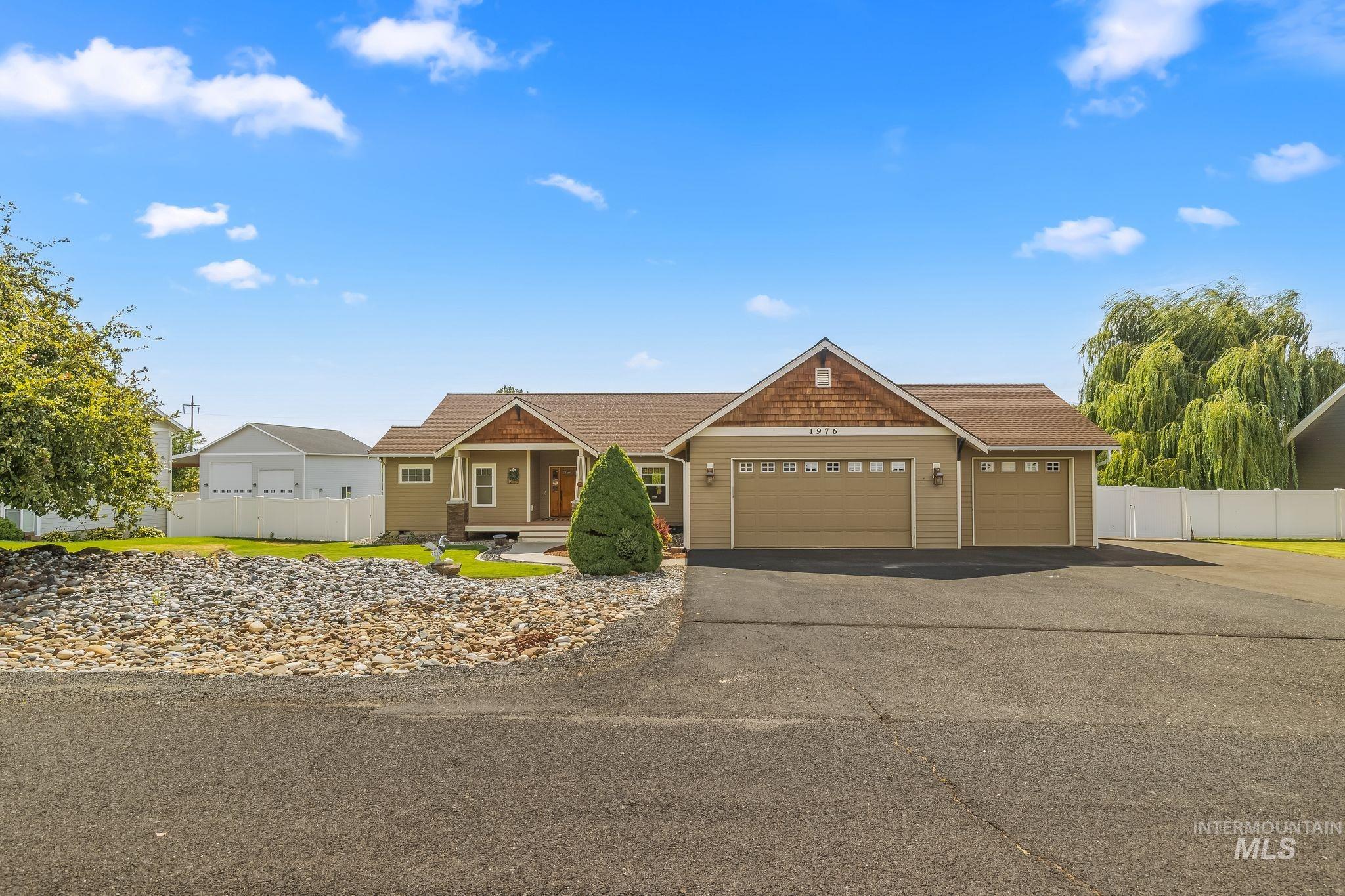 Ranch-style residence featuring a prominent three-car garage, covered entry porch, and a gravel front yard