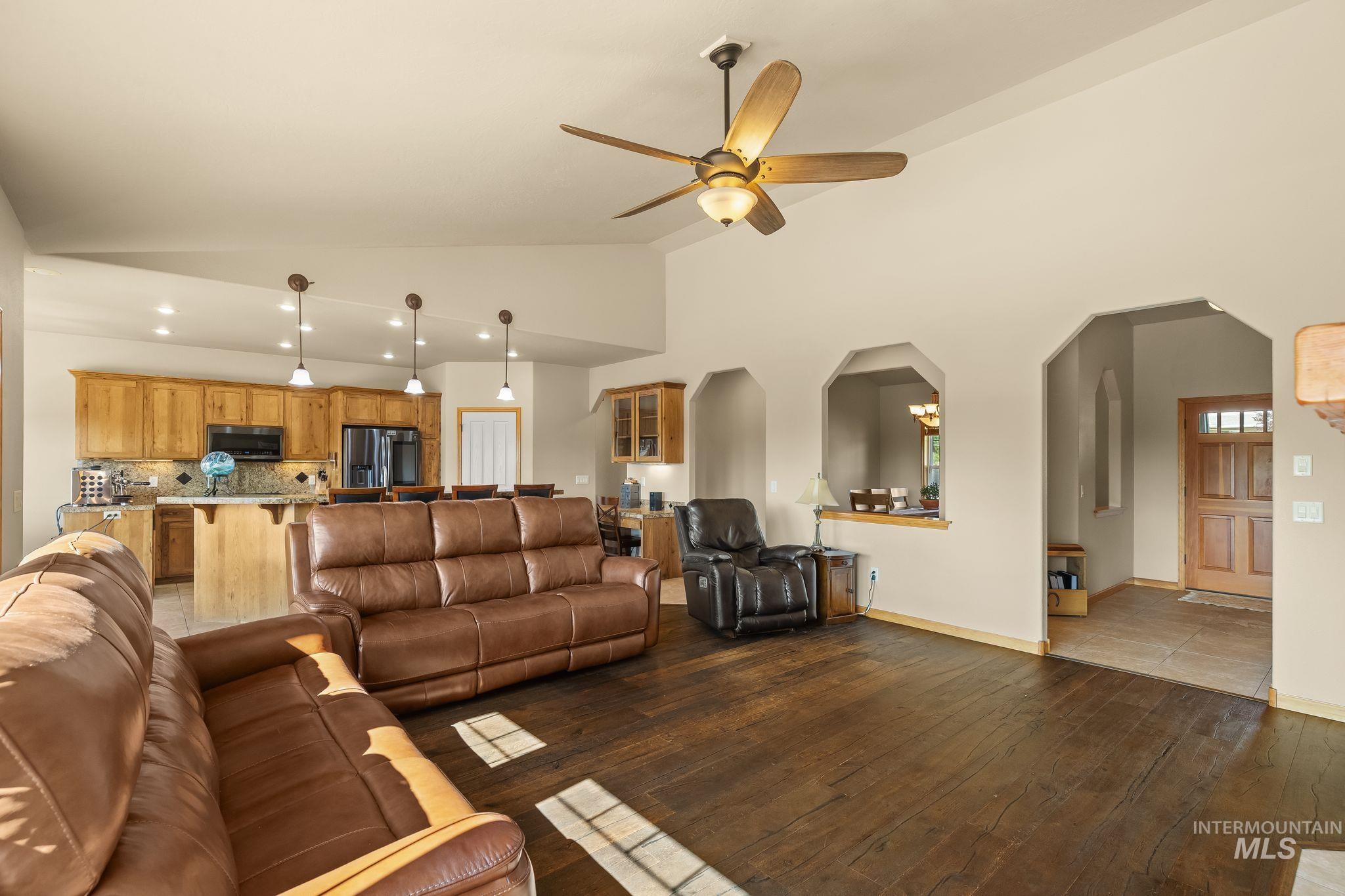 Open-concept living area featuring rich wood-finish flooring, vaulted ceilings with a ceiling fan, and arched doorways