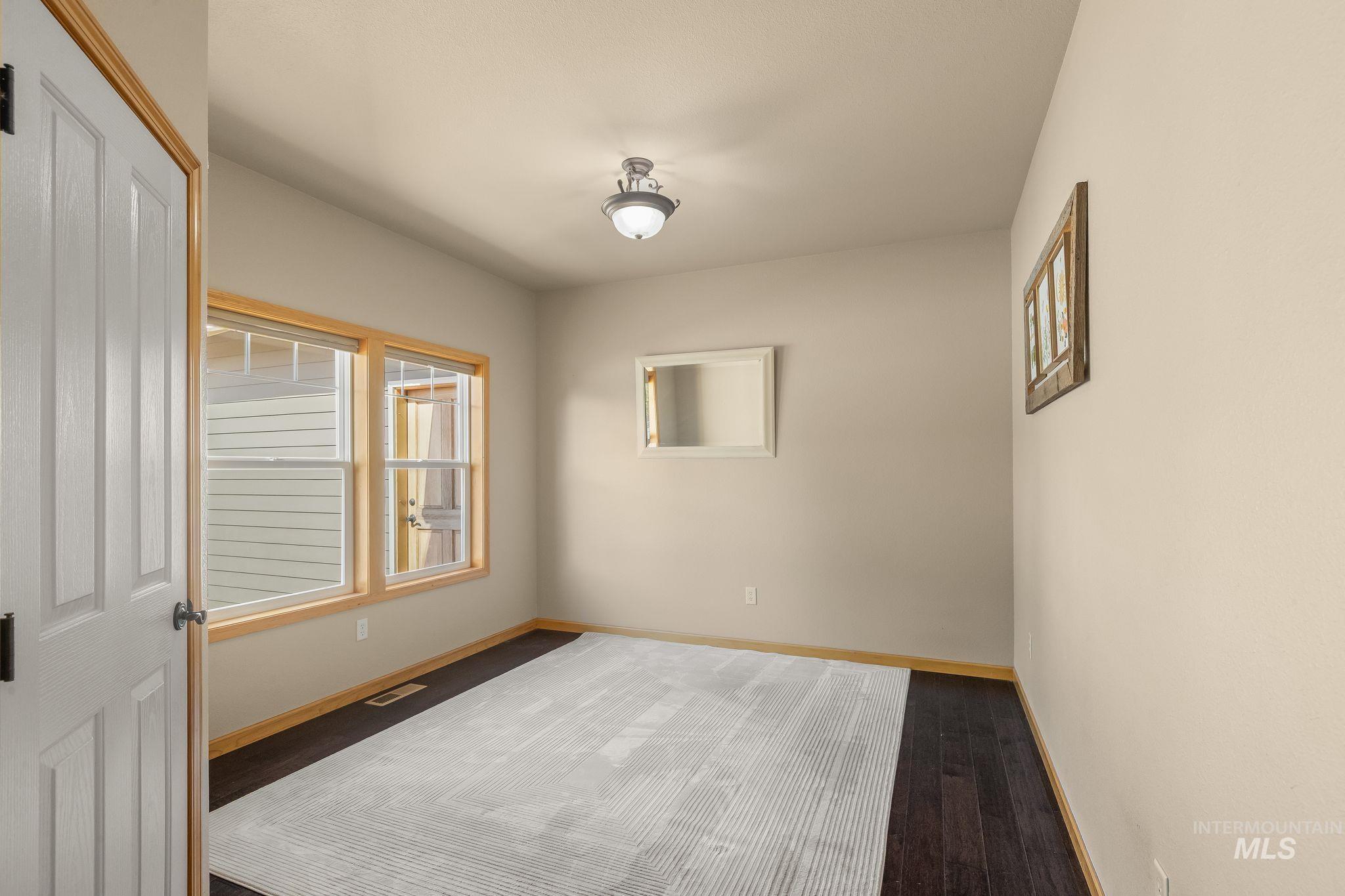 Room featuring dark wood-finish flooring, two large windows with natural wood trim, and a semi-flush mount ceiling light fixture