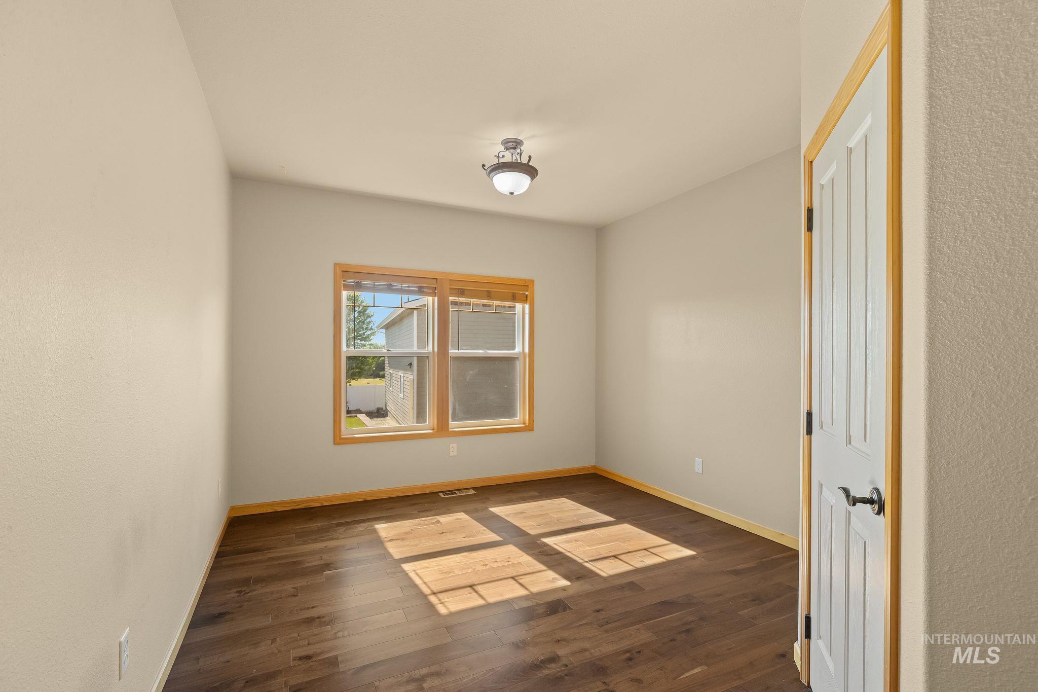 Room featuring wood-finish flooring, light neutral wall tones, a wood-trimmed window, a ceiling-mounted light fixture, and a paneled interior door with wood trim