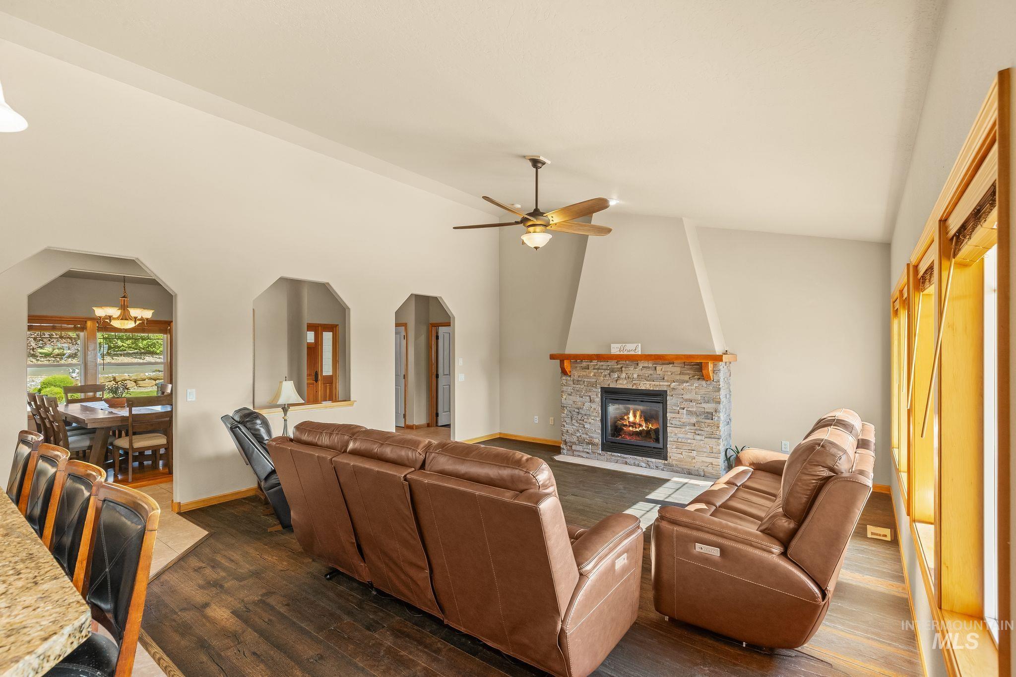 Spacious great room featuring vaulted ceilings, wood-finish flooring, a stone-faced fireplace with a wood mantel, and multiple arched doorways