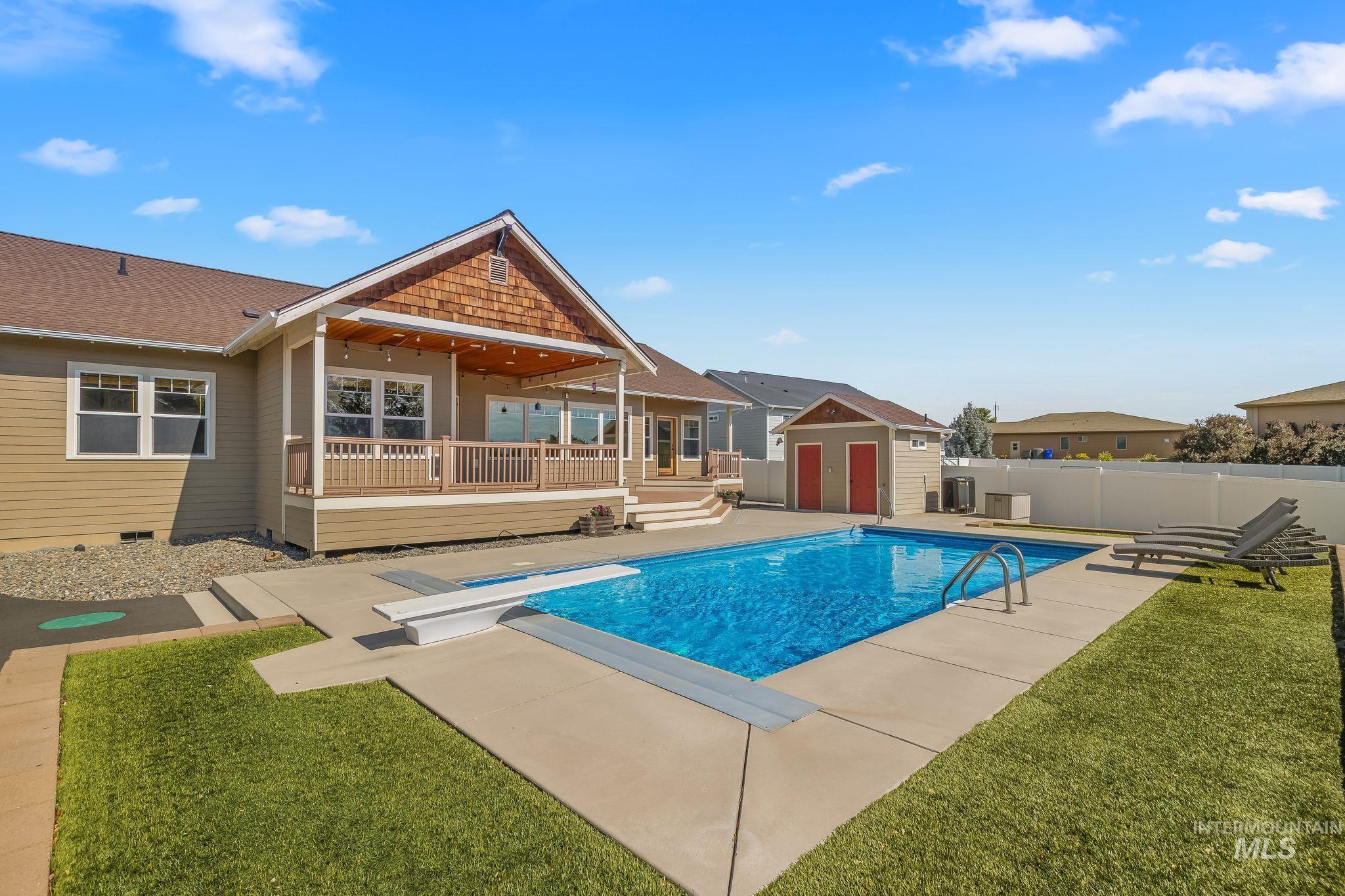 Inviting backyard featuring an in-ground swimming pool with concrete decking, a covered patio with string lighting, and a separate storage shed with red doors