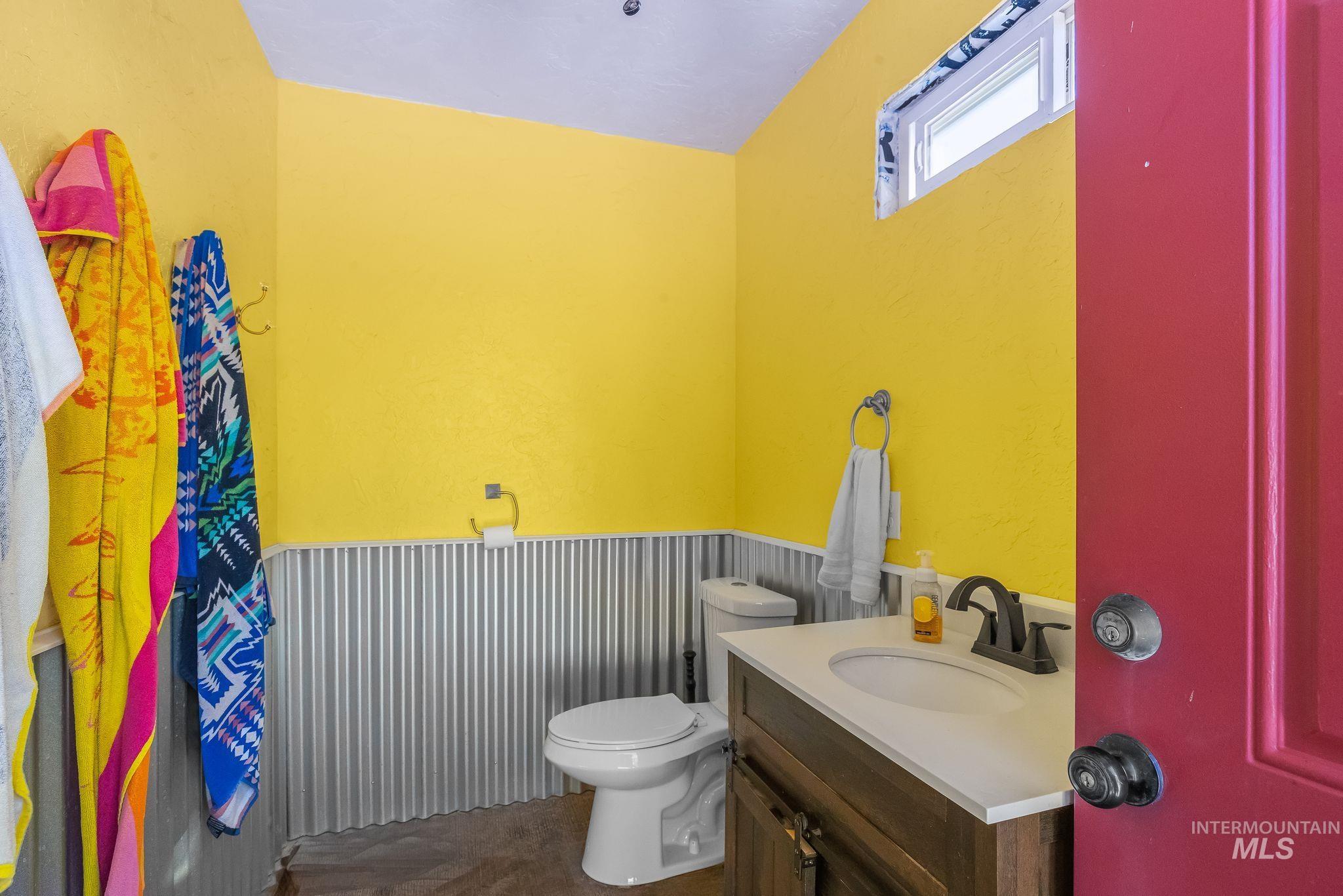 Bathroom featuring a wood vanity with a white countertop and undermount sink, a bronze-finish faucet, corrugated metal wainscoting, and a privacy window