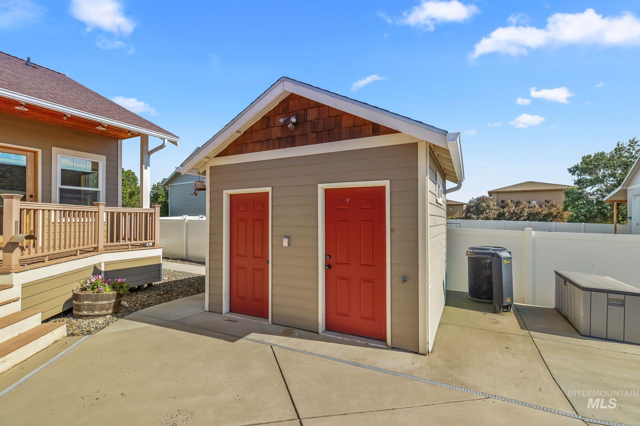 Detached structure with two red doors and wood shingle gable accent, concrete patio, and a privacy fence