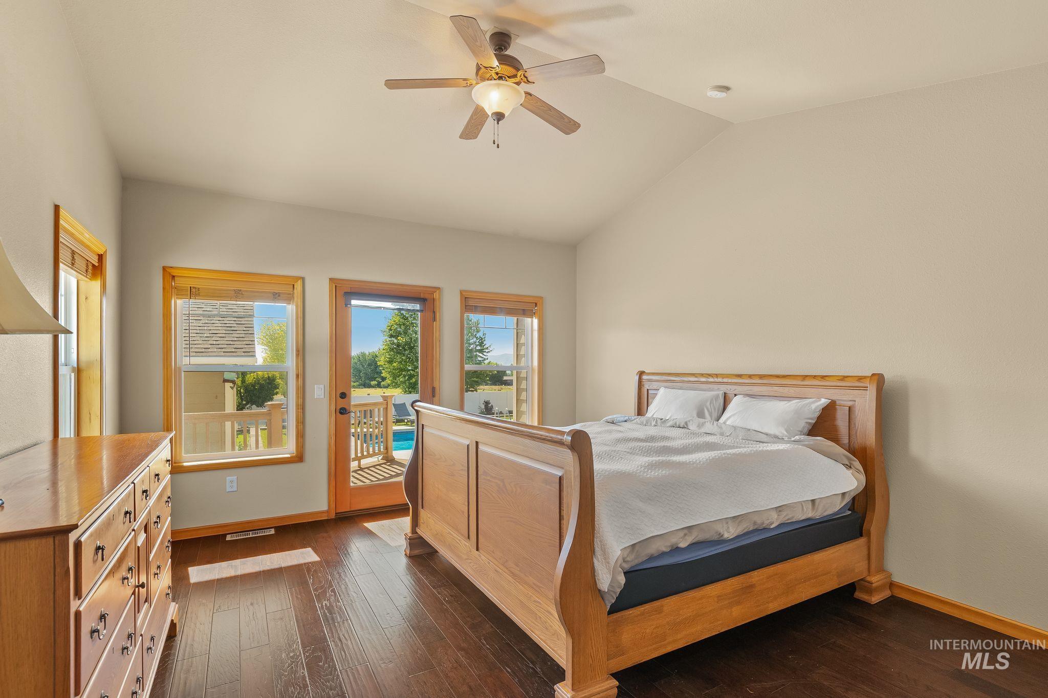 Vaulted ceiling room with wood-finish flooring, featuring a glass-paned door opening to an outdoor deck