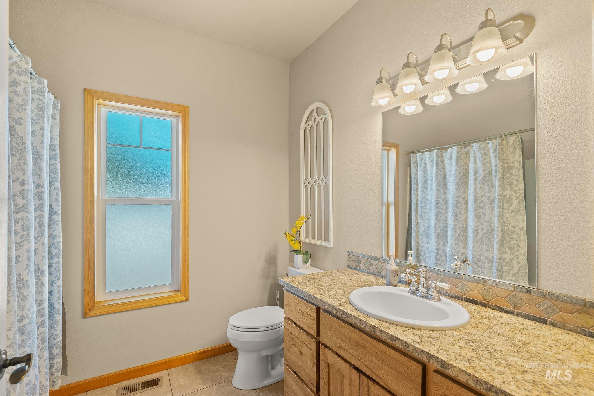 Bathroom featuring a wood-framed window, tile flooring, and a vanity with a light-colored countertop and wooden cabinetry