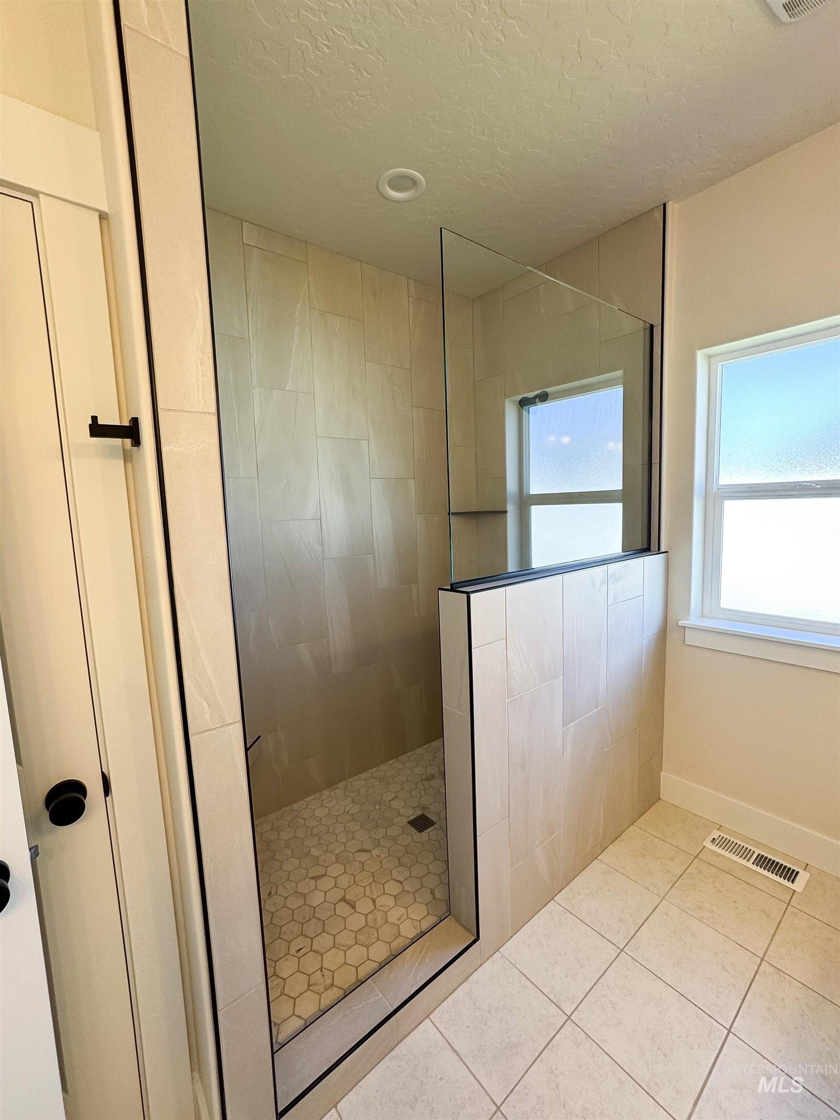 Full bath with a walk in shower, tile patterned flooring, and a textured ceiling