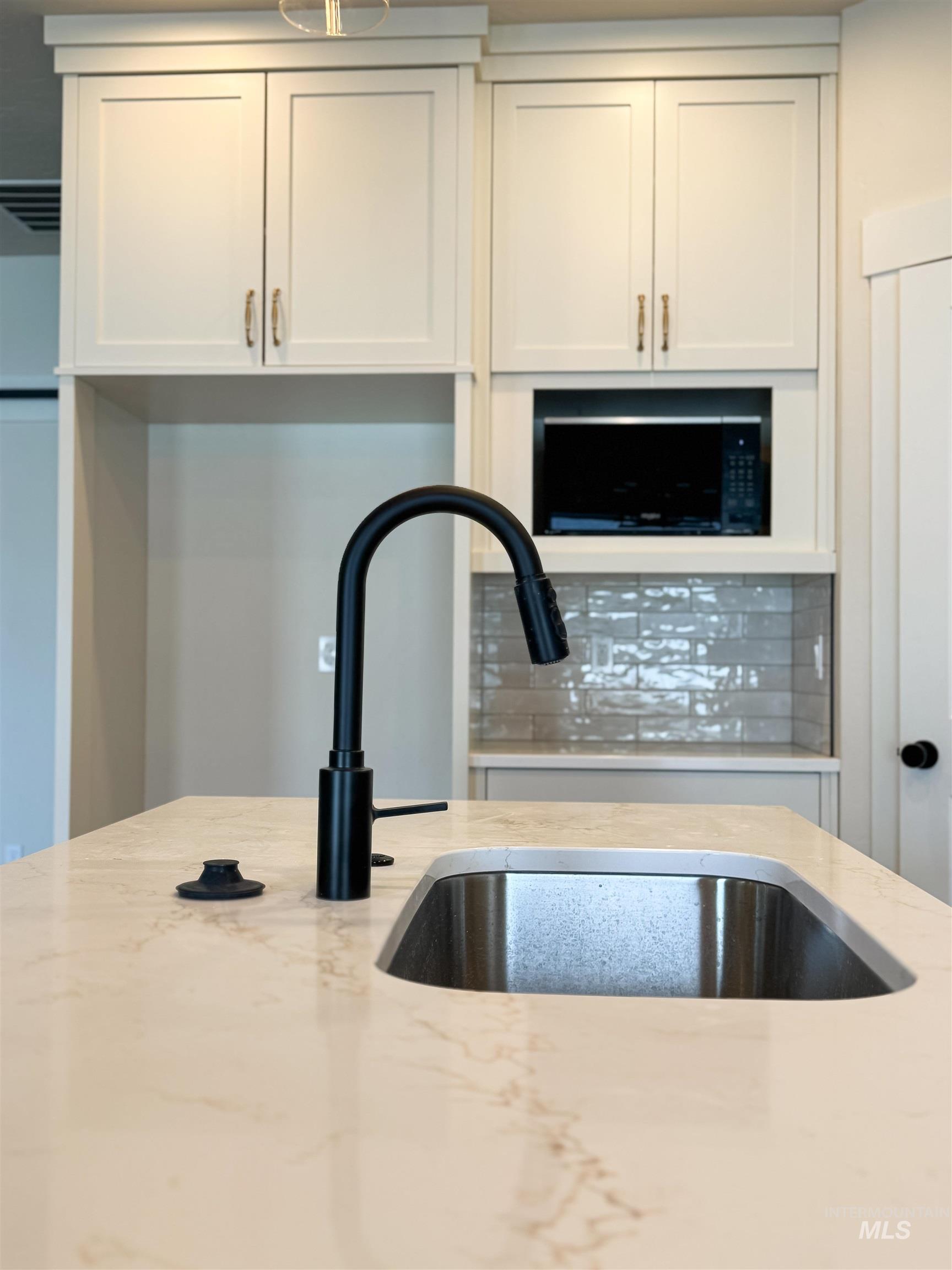 Kitchen view of light stone counters, black microwave, white cabinets, and tasteful backsplash