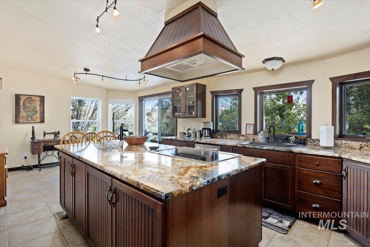 Kitchen with light stone counters, premium range hood, a textured ceiling, and a kitchen island