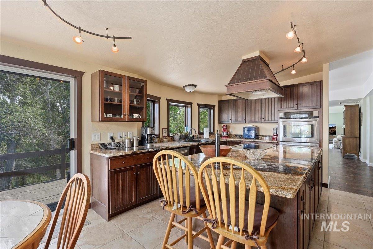 Kitchen with rail lighting, island exhaust hood, light tile patterned flooring, glass insert cabinets, and a center island