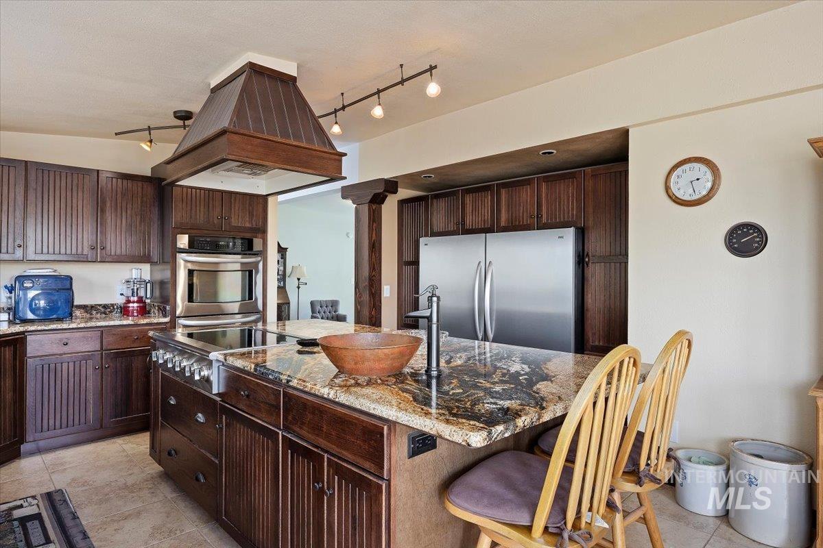 Kitchen featuring stainless steel appliances, a kitchen island, island range hood, light stone countertops, and a breakfast bar