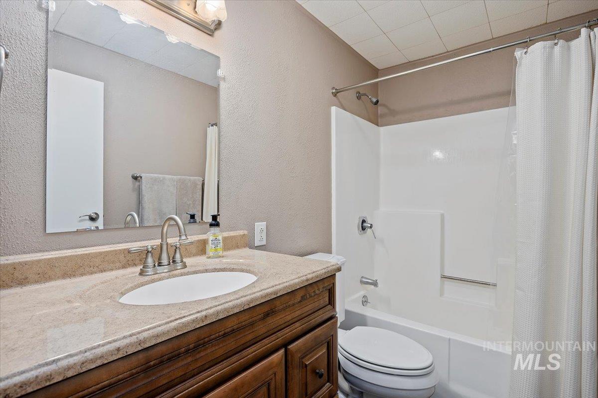 Bathroom featuring shower / bathtub combination with curtain, vanity, and a textured wall