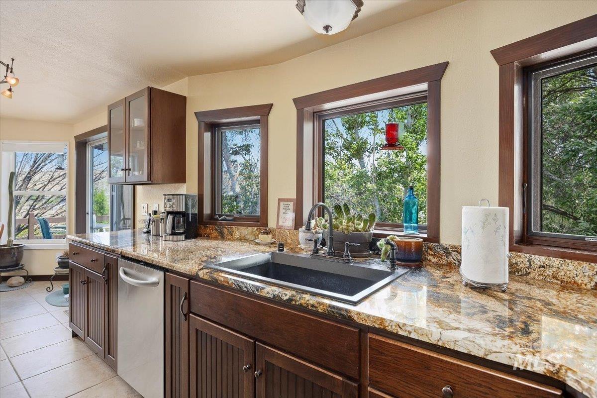 Kitchen featuring glass insert cabinets, dishwasher, light stone countertops, and light tile patterned floors