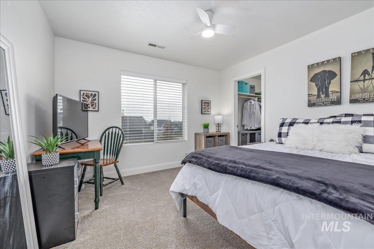 Bedroom with light carpet, a walk in closet, a ceiling fan, and an office area