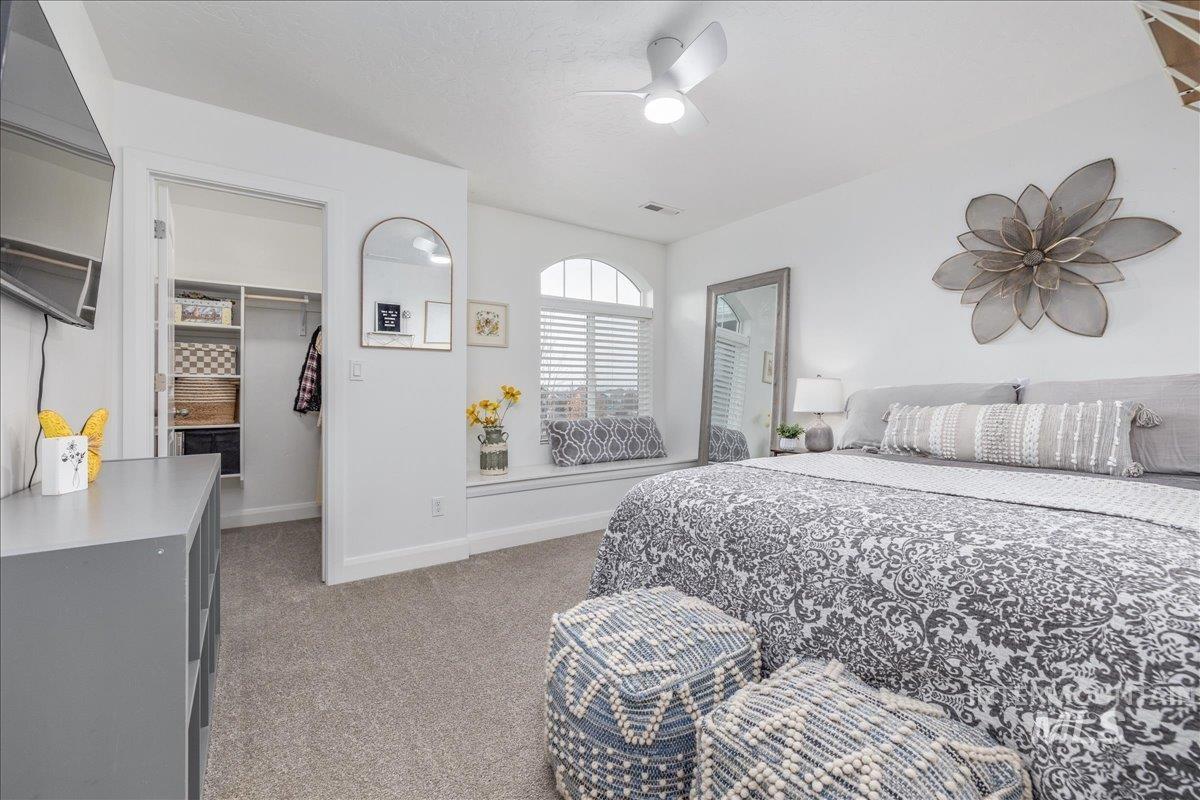 Bedroom featuring a walk in closet, light carpet, and a ceiling fan