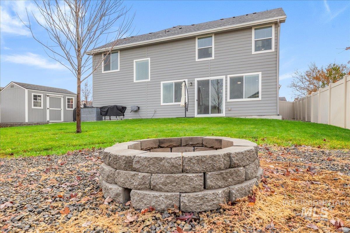 Back of property with a fire pit, a fenced backyard, and a storage shed