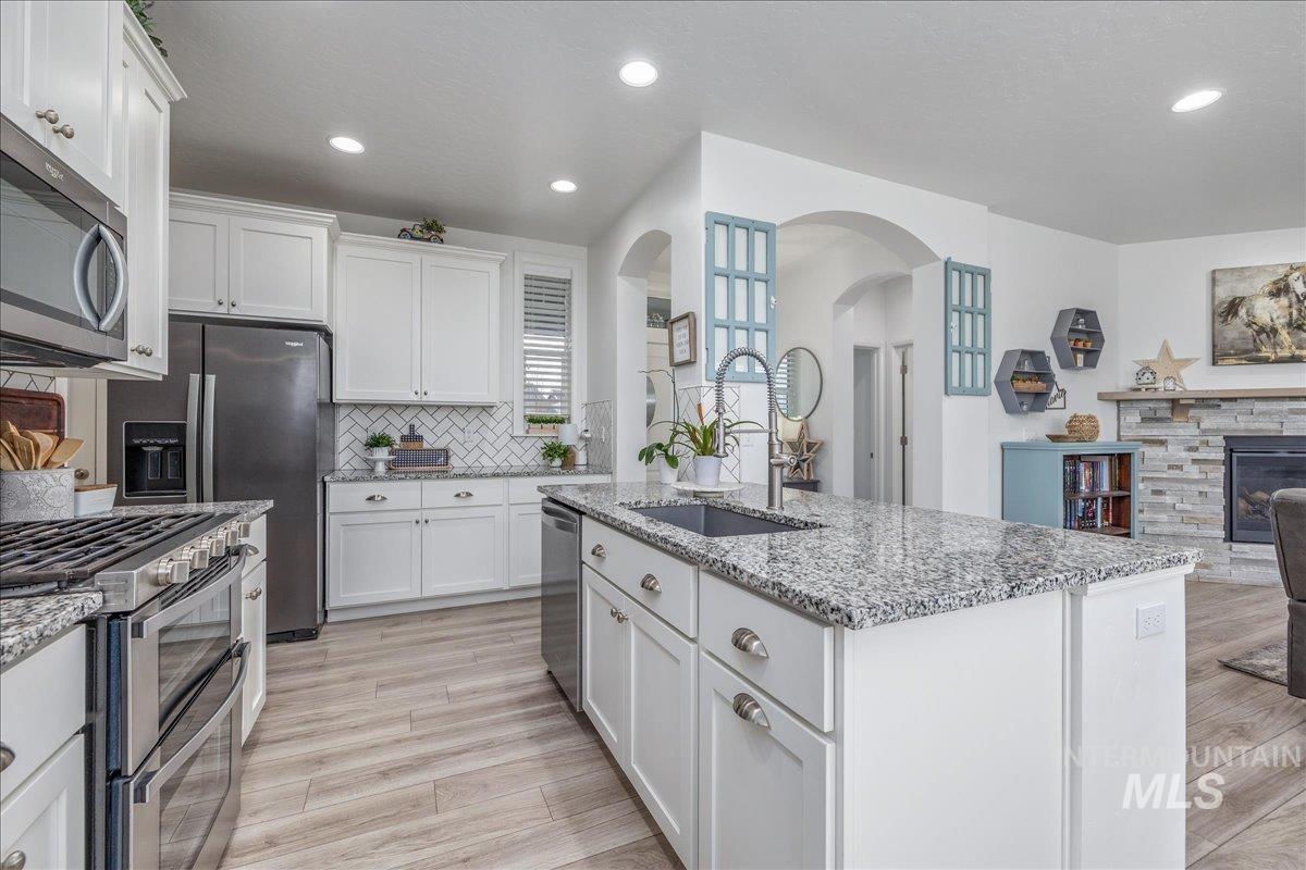 Kitchen with appliances with stainless steel finishes, white cabinetry, a fireplace, open floor plan, and arched walkways
