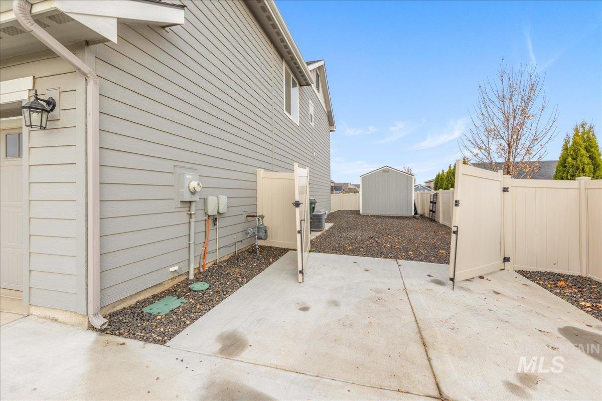 View of side of home featuring a gate, a fenced backyard, a patio area, and a storage unit