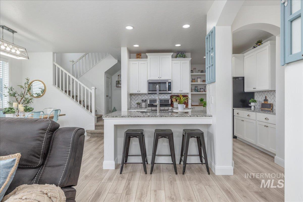 Kitchen featuring a breakfast bar area, white cabinetry, light stone counters, stainless steel appliances, and recessed lighting