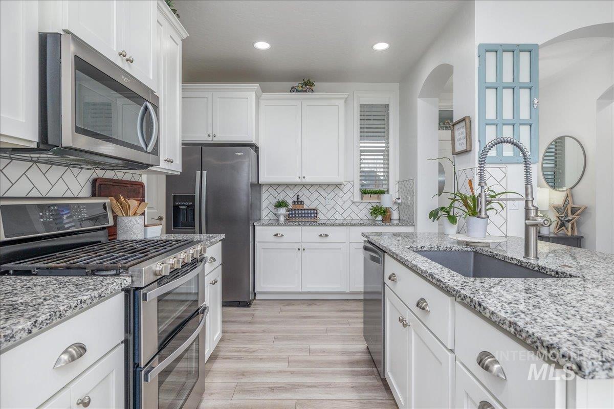 Kitchen featuring stainless steel appliances, white cabinetry, light stone countertops, recessed lighting, and light wood finished floors
