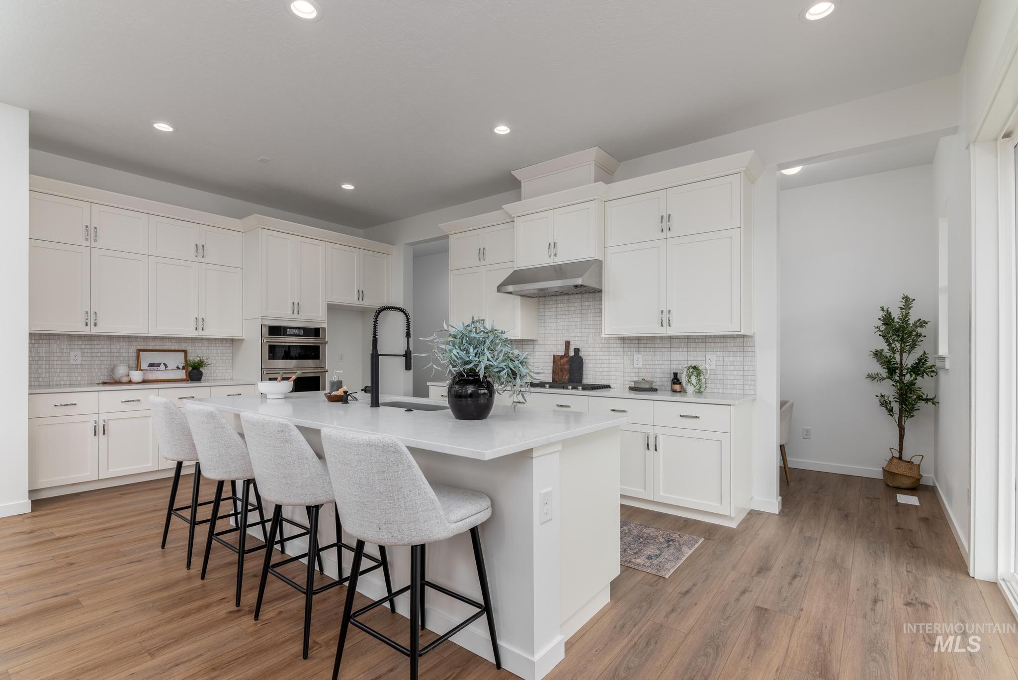 Kitchen with a kitchen bar, white cabinetry, an island with sink, light wood finished floors, and recessed lighting