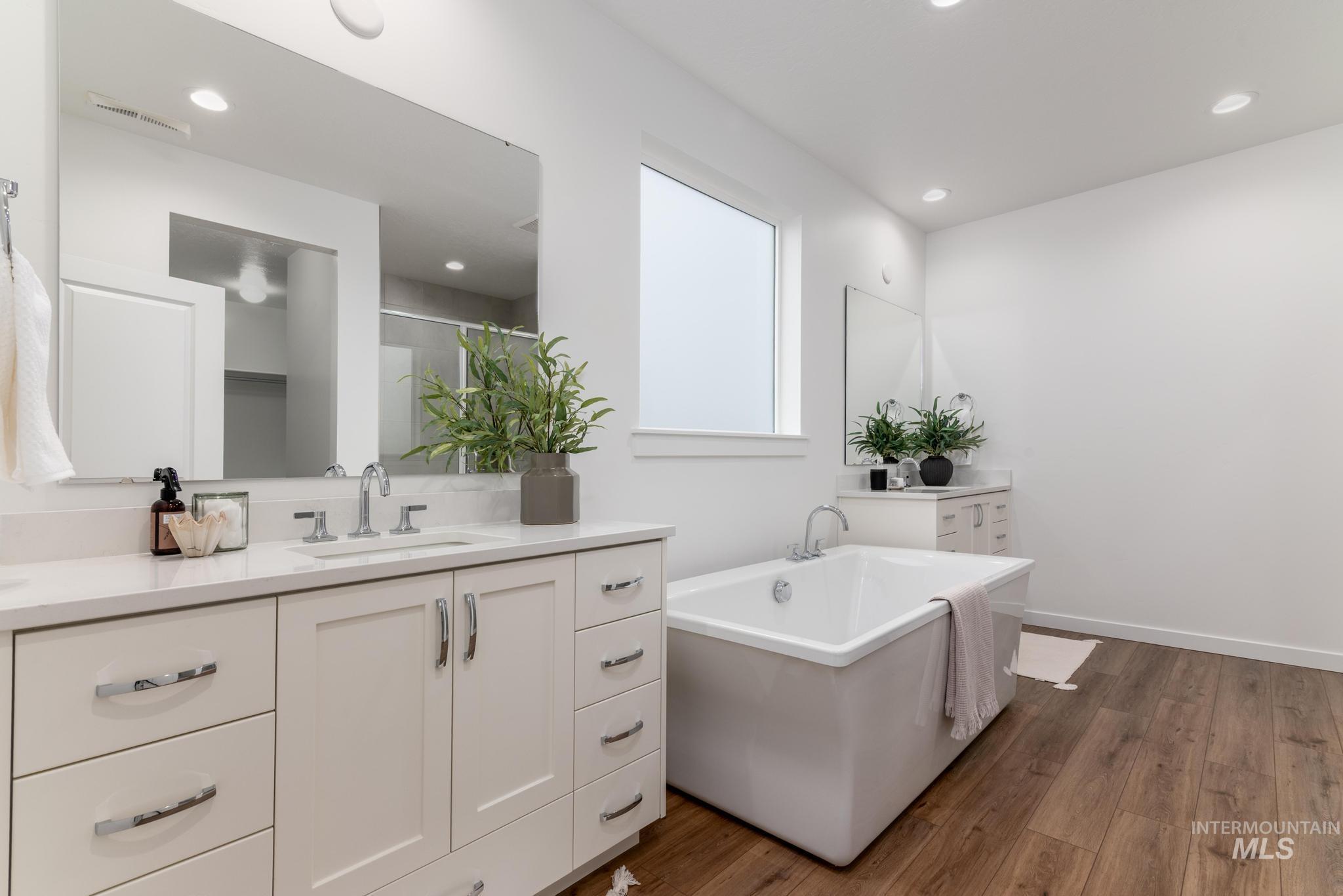 Full bathroom featuring two vanities, dark wood-style flooring, a freestanding tub, a stall shower, and recessed lighting