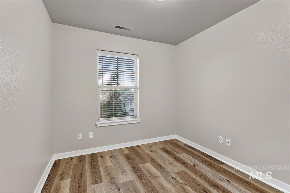 Interior room featuring wood-finish flooring, light neutral wall tones, white baseboards, and a window with horizontal blinds