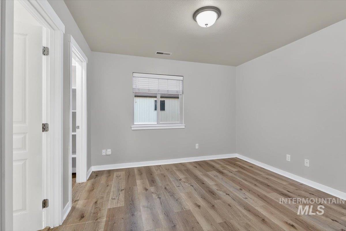 Room featuring wood-finish flooring, light gray walls, white baseboards, and a window with blinds