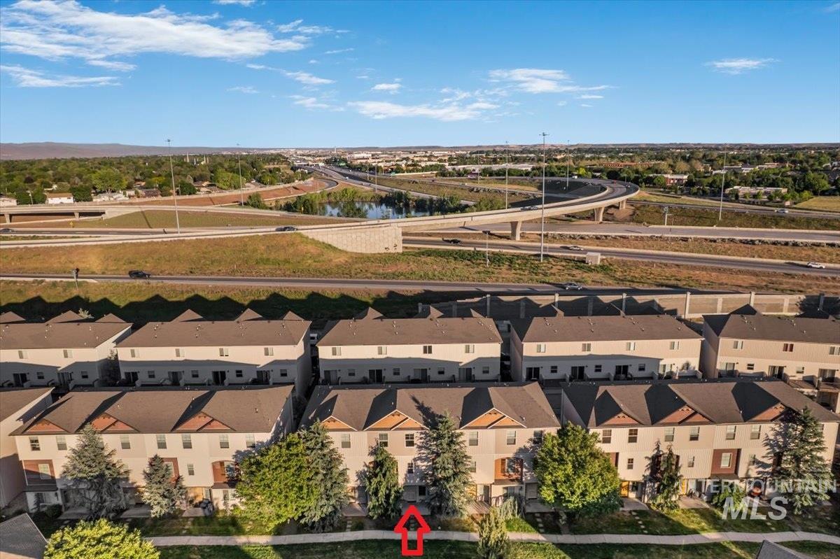 Multi-story townhome exterior featuring an attached garage, mature trees, and a landscaped front yard