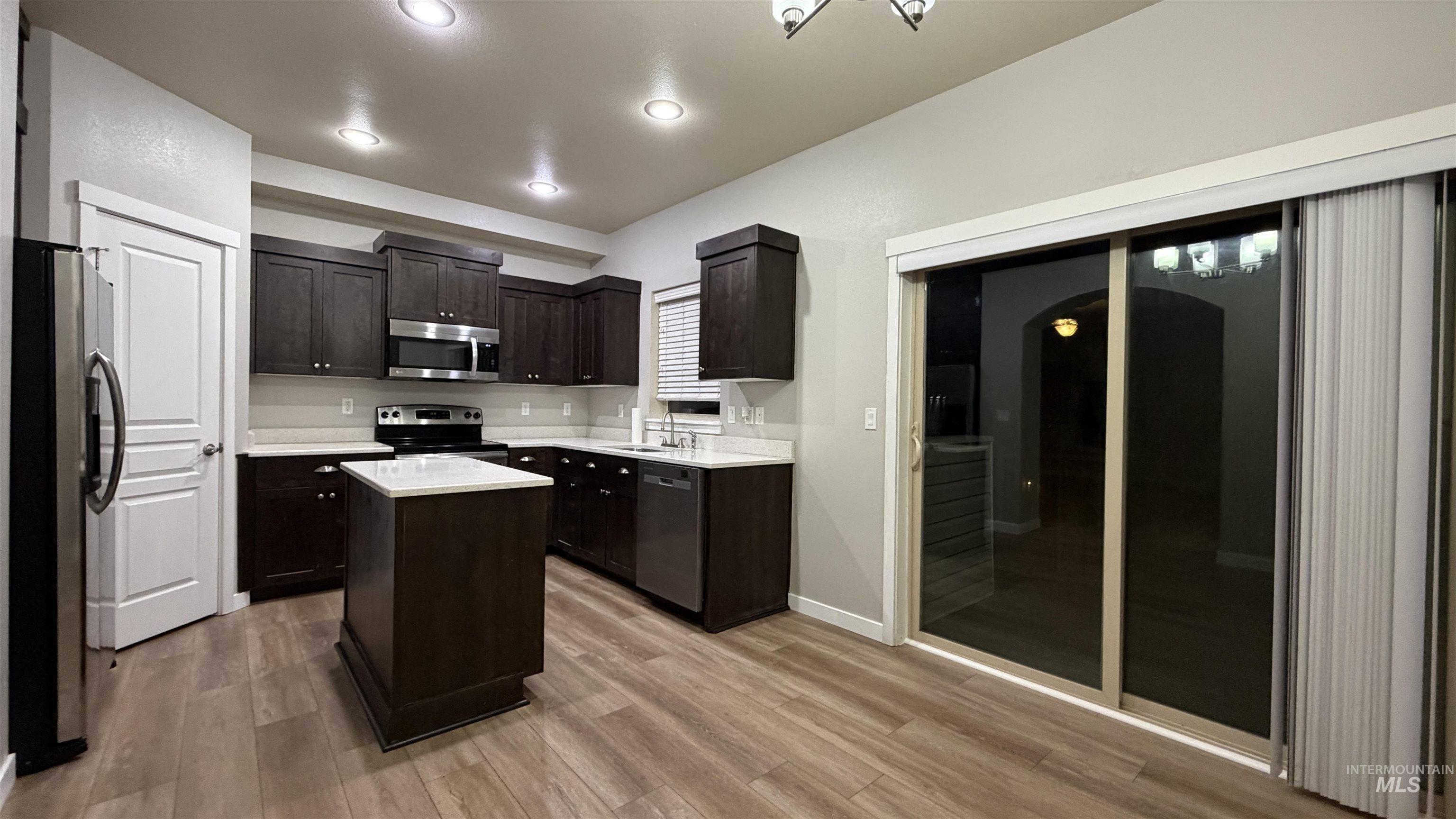 Modern kitchen featuring dark wood cabinetry, stainless steel appliances, and a central island with a light-toned countertop