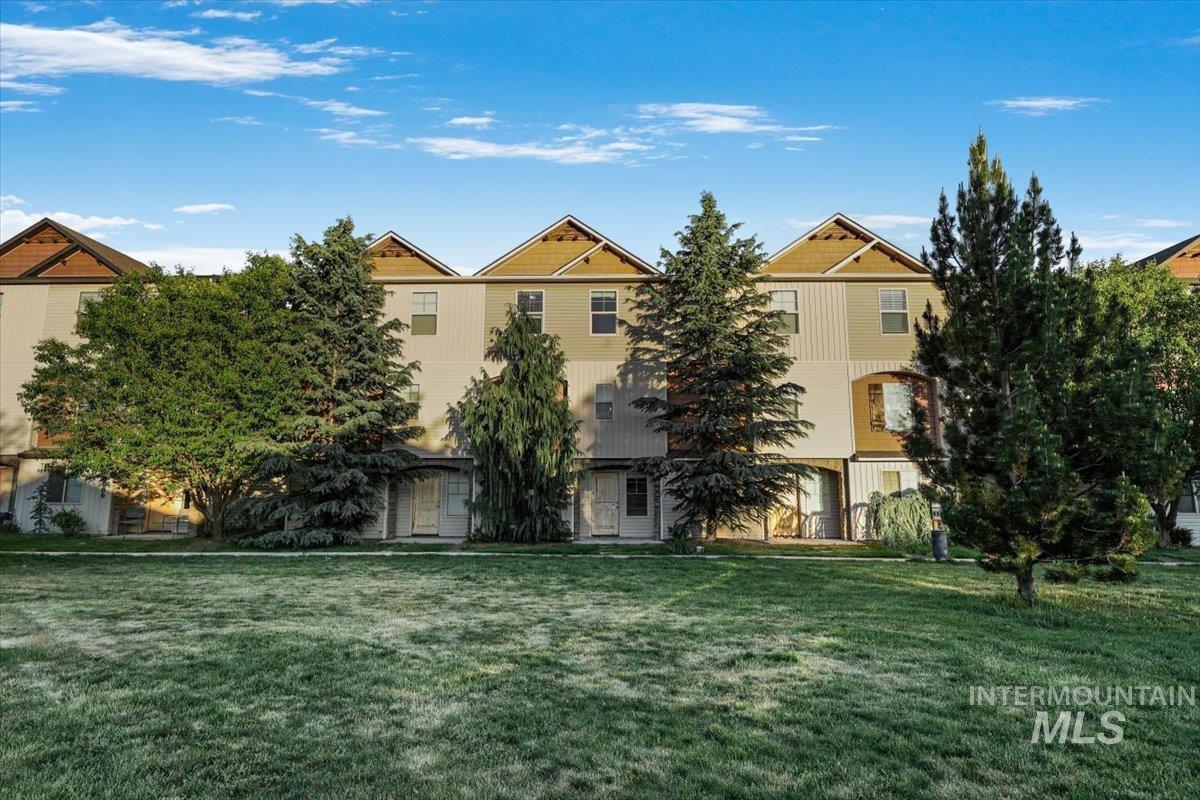 Townhome exterior featuring multiple gabled rooflines, light-toned siding, and mature evergreen trees