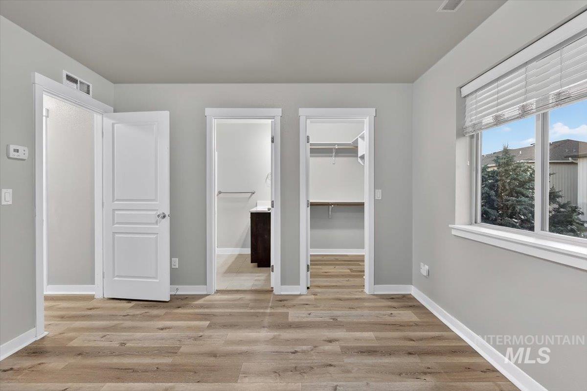 Spacious room featuring wood-finish flooring, light grey walls, and a large window with white blinds