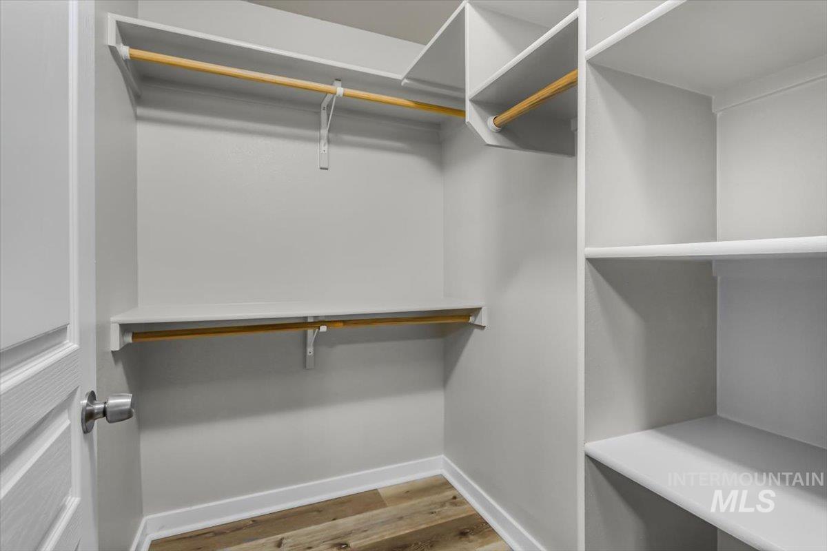 Walk-in closet featuring built-in shelving, multiple hanging rods, light gray walls, white baseboards, and wood-finish flooring