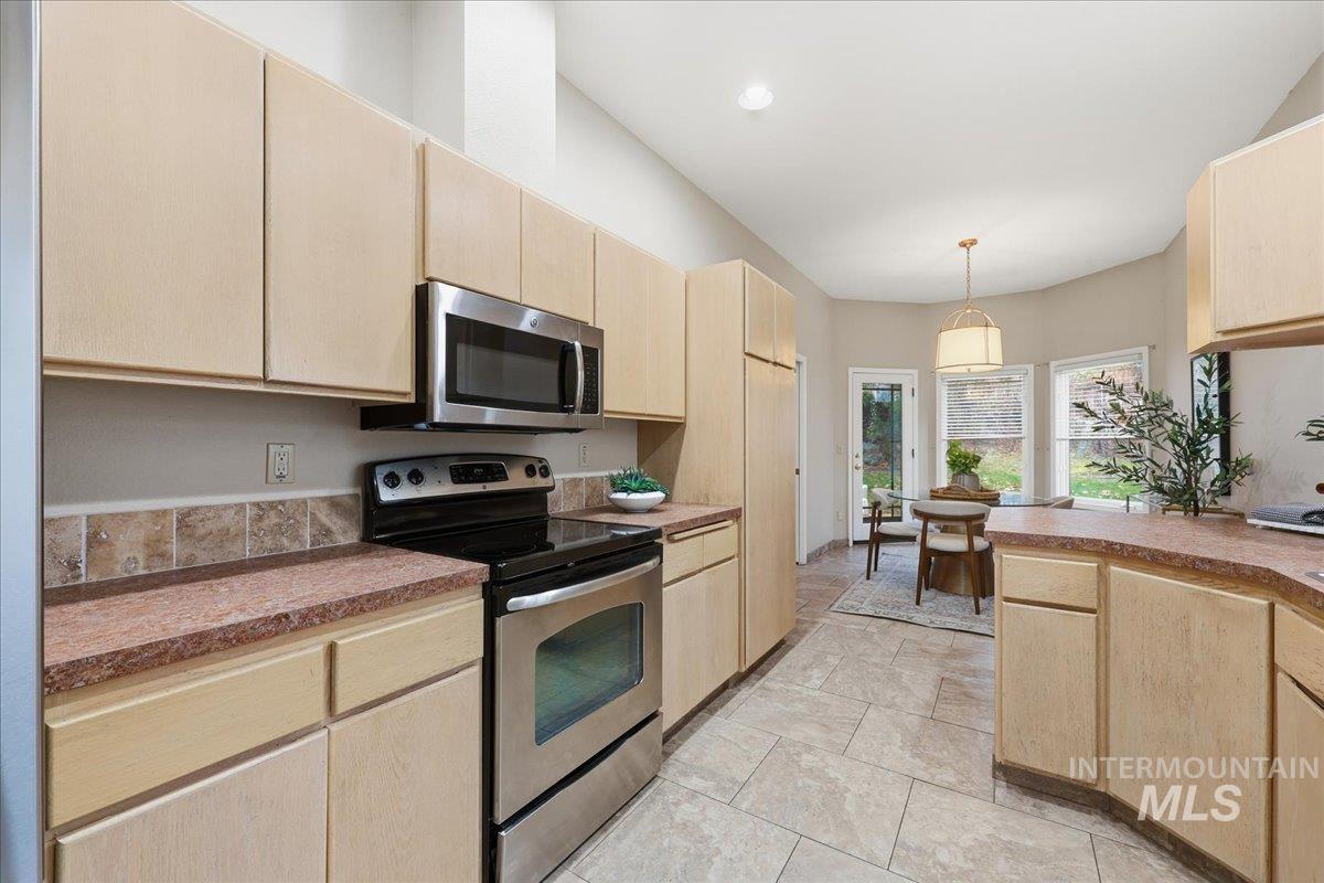 Kitchen featuring appliances with stainless steel finishes, light brown cabinets, decorative light fixtures, and light countertops