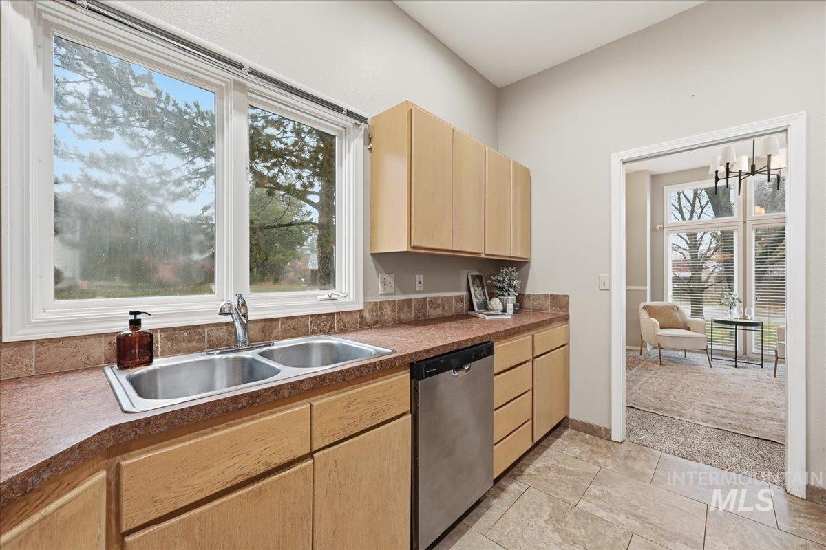 Kitchen with light brown cabinetry, stainless steel dishwasher, plenty of natural light, and dark countertops