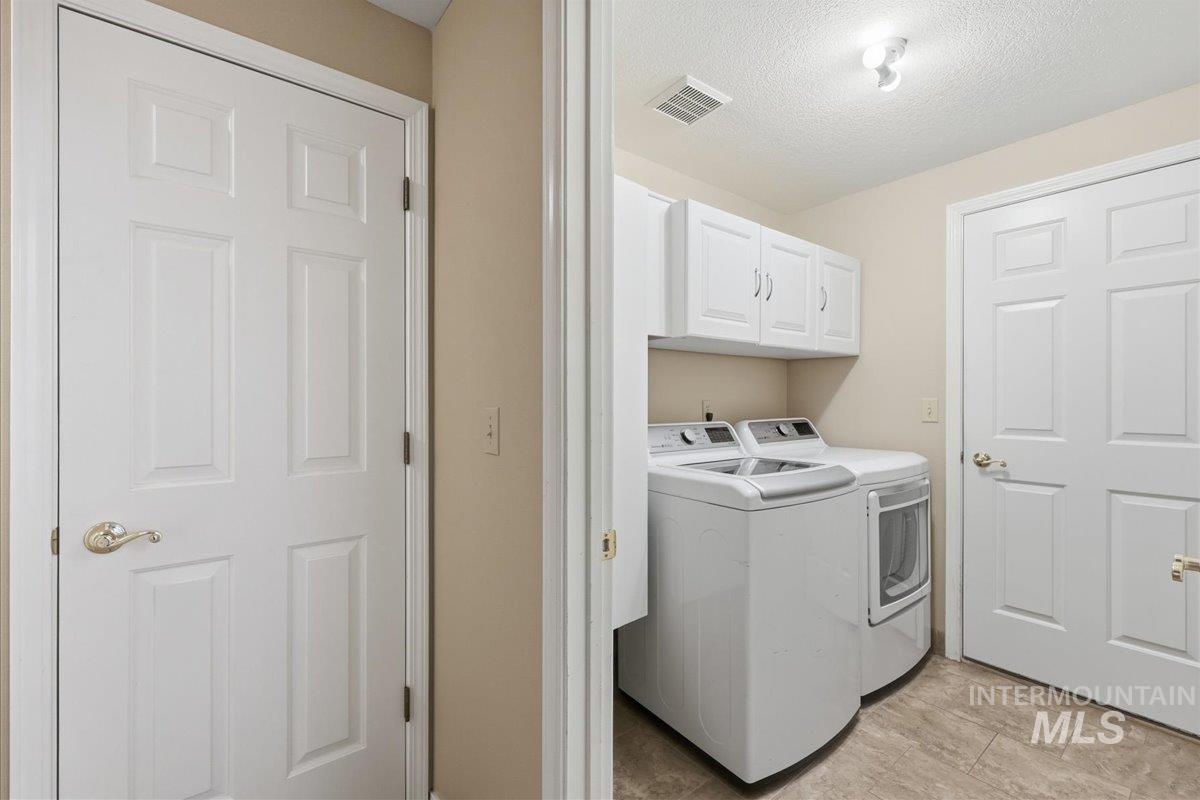 Laundry room featuring washer and dryer, a textured ceiling, and cabinet space